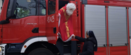Mikołaj wysiadający z wozu strażackiego w asyście siostry zakonnej