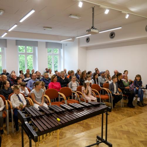 Koncerty uczniów klasy pierwszej. Zdjęcie przedstawiające widok publiczności zgromadzonej na koncercie uczniów klas pierwszych. Zdjęcie wykonane ze sceny. Na pierwszym planie widoczny stojący na scenie ksylofon.
