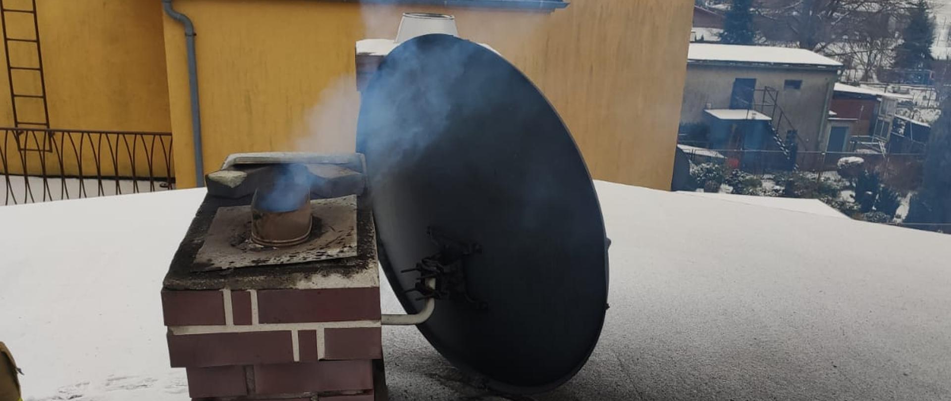 Na zdjęciu znajduje się dymiący komin oraz antena satelitarna