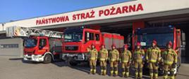 Zdjęcie przedstawia siedmiu strażaków i trzy wozy pożarnicze