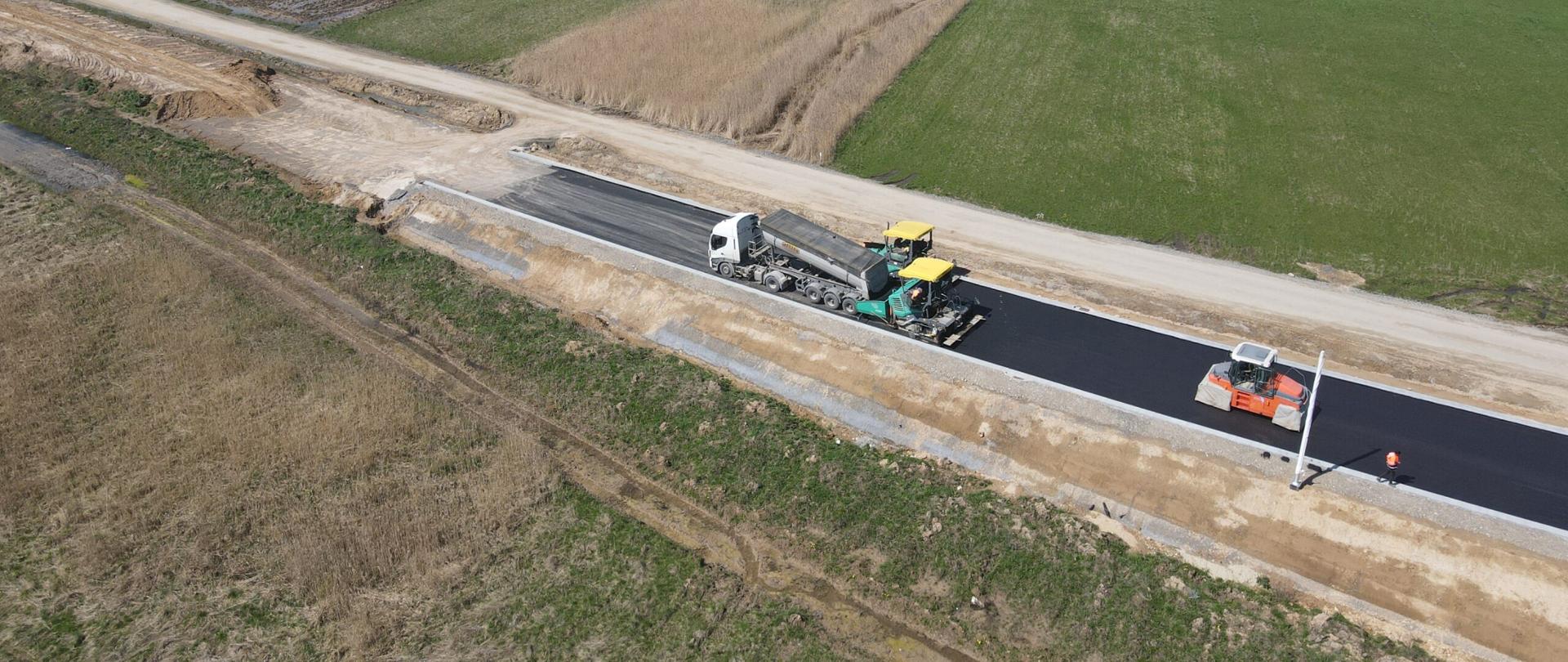 DK9 obwodnica Ostrowca Świętokrzyskiego - układanie nawierzchni na jednojezdniowej drodze, rozściełacz, walec, samochód ciężarowy 
