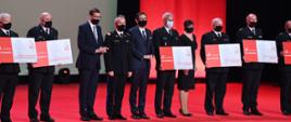 Na scenie 10 uczestników gali, w tym premier, komendant główny , prezes PKN ORLEN, 6 osób trzyma symboliczne czeki