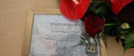 Beżowa ławka, na niej pamiątkowy dyplom dla odchodzącego na emeryturę pracownika oraz bukiet kwiatów. 