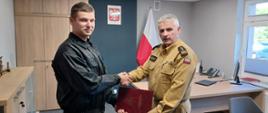 Komendant Powiatowy Państwowej Straży Pożarnej w Człuchowie st. bryg. Radosław Batruch stoi w gabinecie i wręcza akt mianowania na stanowisko dowódcy zmiany st. asp. Dariuszowi Buczko.