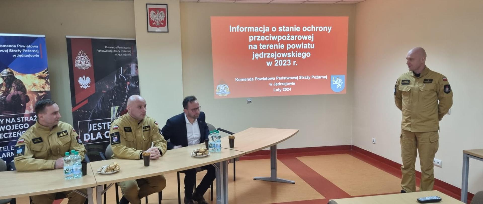Przy stole prezydialnym widać od lewej zastępcę komendanta powiatowego PSP w Jędrzejowie bryg. Tomasza Szymańskiego, zastępcę świętokrzyskiego komendanta wojewódzkiego PSP w Kielcach st. bryg. Grzegorza Rajcę, starostę jędrzejowskiego. Prezentację przedstawia komendant powiatowy PSP w Jędrzejowie mł. bryg. Mariusz Stolarczyk.