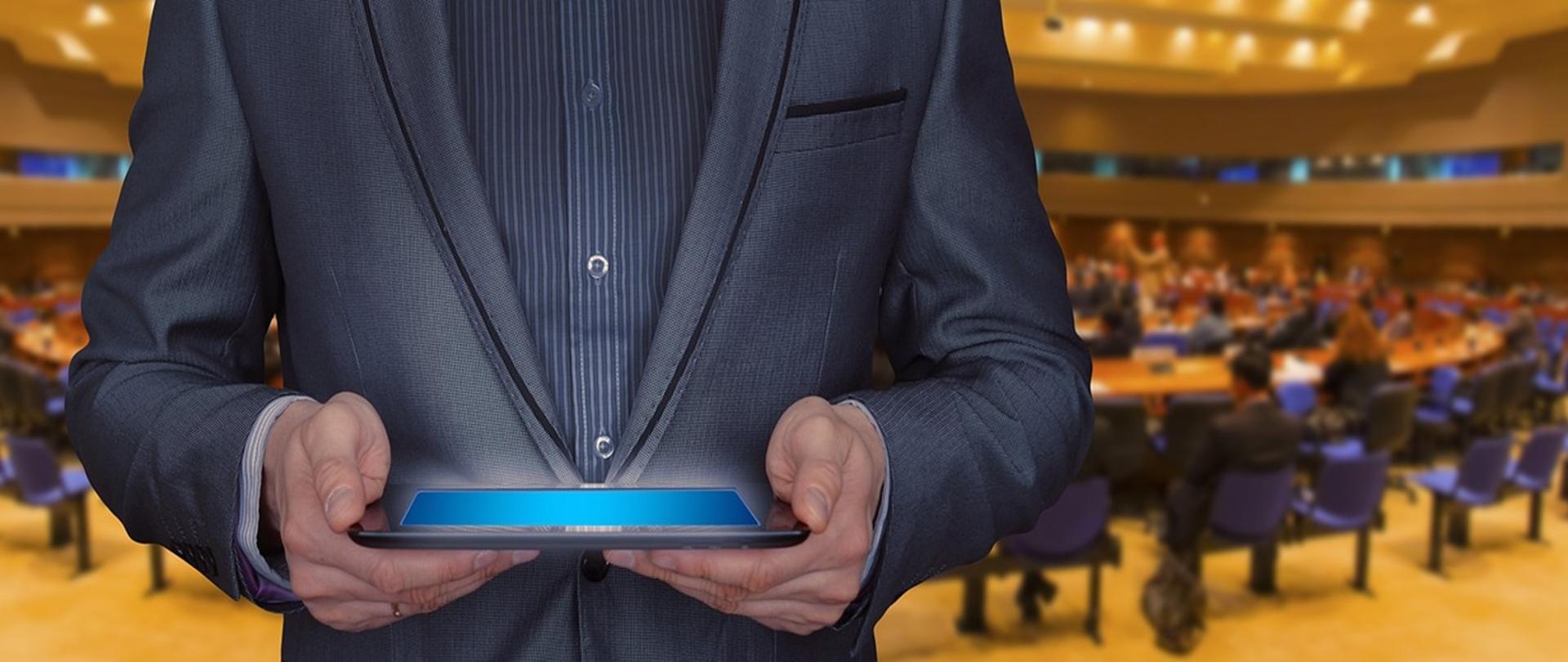 Elegancko ubrany mężczyzna trzymający tablet na tle konferencji