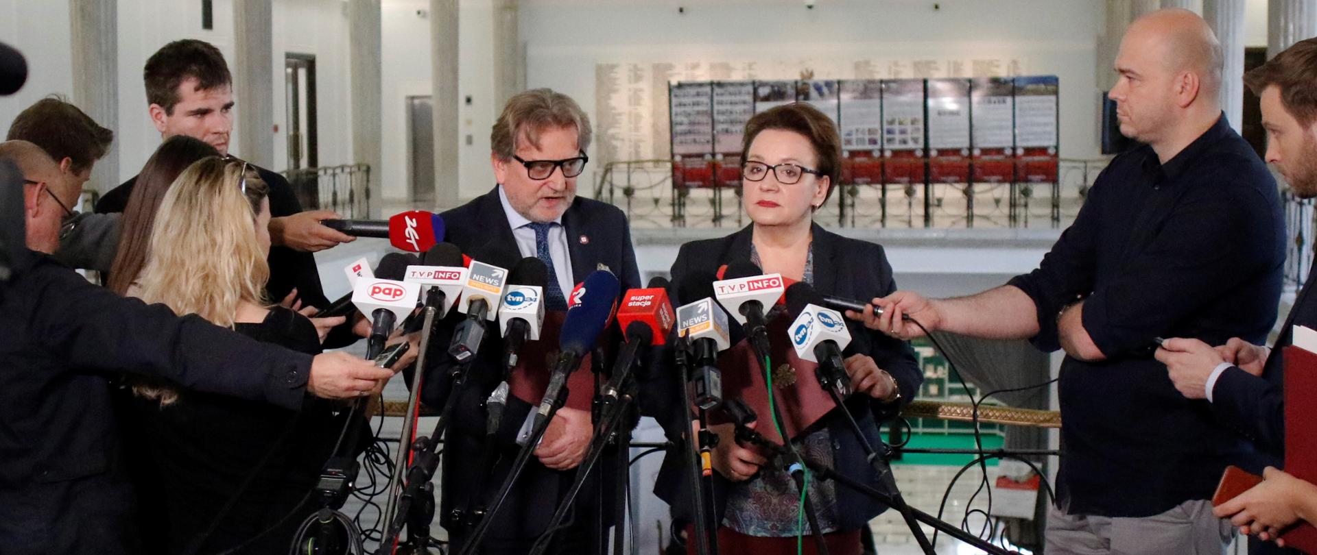 Konferencja prasowa Minister Edukacji Narodowej i Głównego Inspektora Sanitarnego. Ministrowie stoją przed mikrofonami. Obok stoją dziennikarze. 