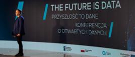 Grzegorz Zajączkowski z Kancelarii Prezesa Rady Ministrów wypowiada się do uczestników konferencji. W tle napis: Future is data. Przyszłość to dane. Konferencja o otwartych danych.