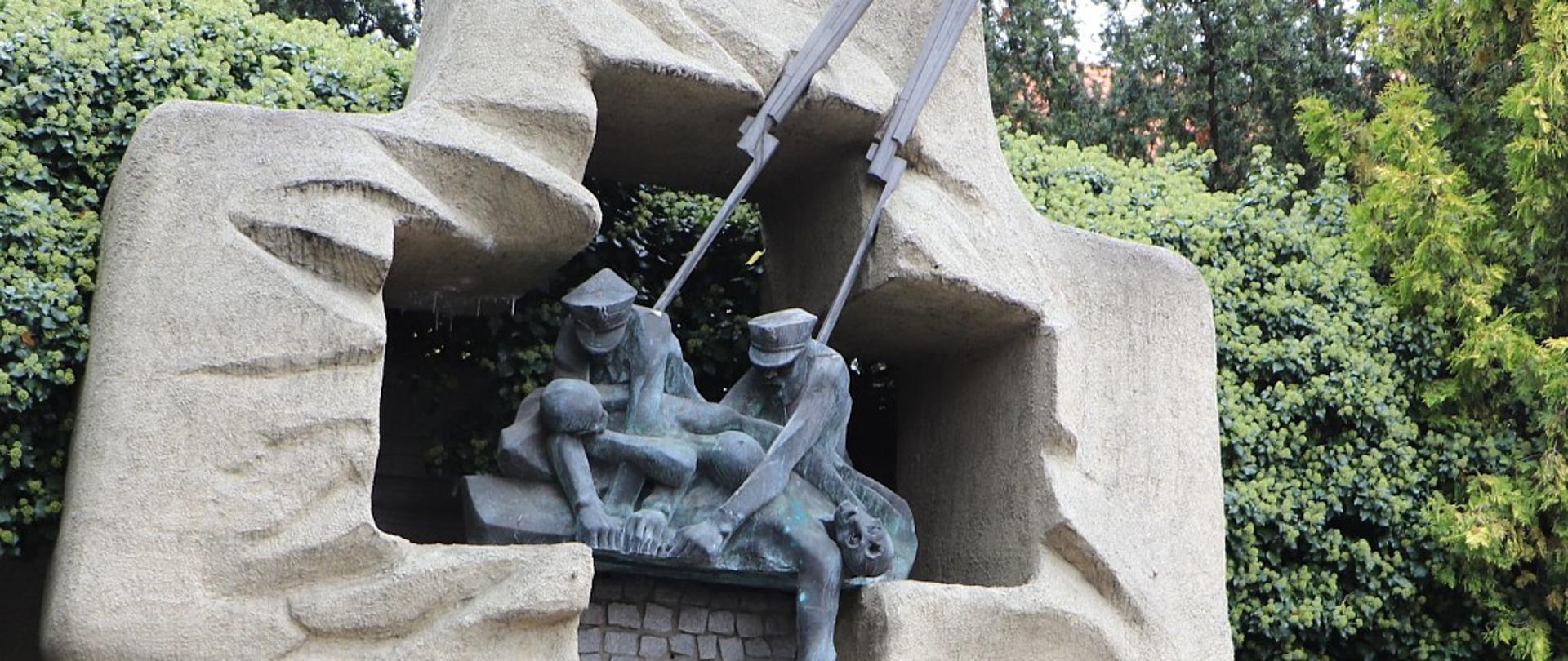 Na zdjęciu pomnik Zbrodni Katyńskiej w ogrójcu klasztoru oo. Jezuitów. Zdjęcie wykonane w ciągu dnia. Na dole widać wiązanki kwiatów.