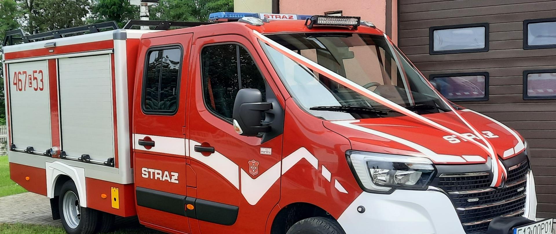 lekki samochód ratowniczo-gaśniczy za pojazdem brama wjazdowa i ściana budynku oraz drzewa