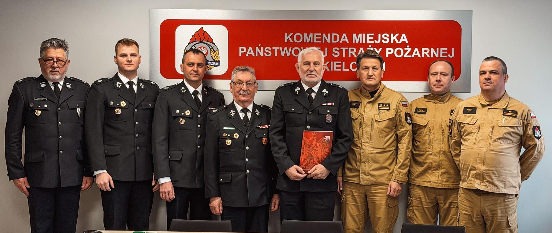 Fotografia przedstawia funkcjonariuszy Komendy Miejskiej PSP w Kielcach wraz z Komendantem Miejskim i druhów OSP Bilcza ustawionych do pamiątkowego zdjęcia podczas przekazania drabiny mechanicznej.