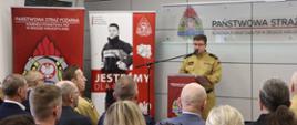Komendant Powiatowy PSP w Środzie Wielkopolskiej bryg. Maciej Kaczmarek przedstawia informację roczną podsumowującą działalność komendy za 2024 r. Przemawia na mównicy przez zgromadzonymi gośćmi oraz pracownikami i funkcjonariuszami tutejszej komendy 