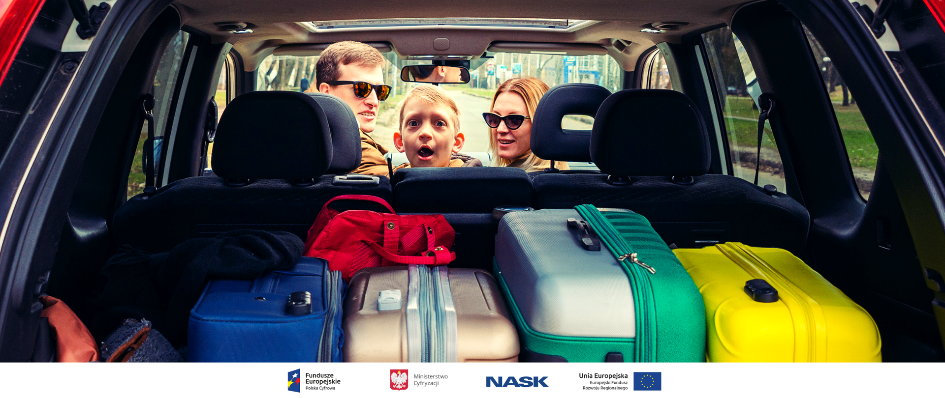 Rodzina siedzi w samochodzie. Widok przez bagażnik. Na pierwszym planie walizki
