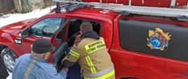 Strażak pomaga starszym ludziom wejść do pojazdu.