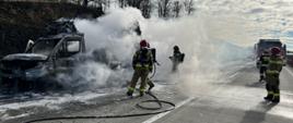 strażacy gaszący pojazd typu bus, widoczne zadymienie, działania prowadzone na autostradzie