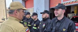 uroczysta zmiana służby, strażacy w ubraniach koszarowych stoją w szeregu, komendant powiatowy wręcza list gratulacyjny i ściska rękę wyróżnionego strażaka