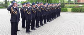 Zdjęcie przedstawia strażaków stojących w szyku podczas obchodów dnia strażaka na placu przed komendą