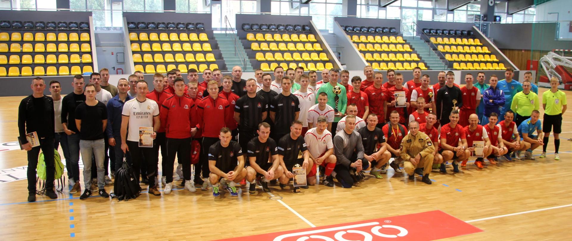 Piłkarze stoją w dwuszeregu na parkiekie hali sportowej.