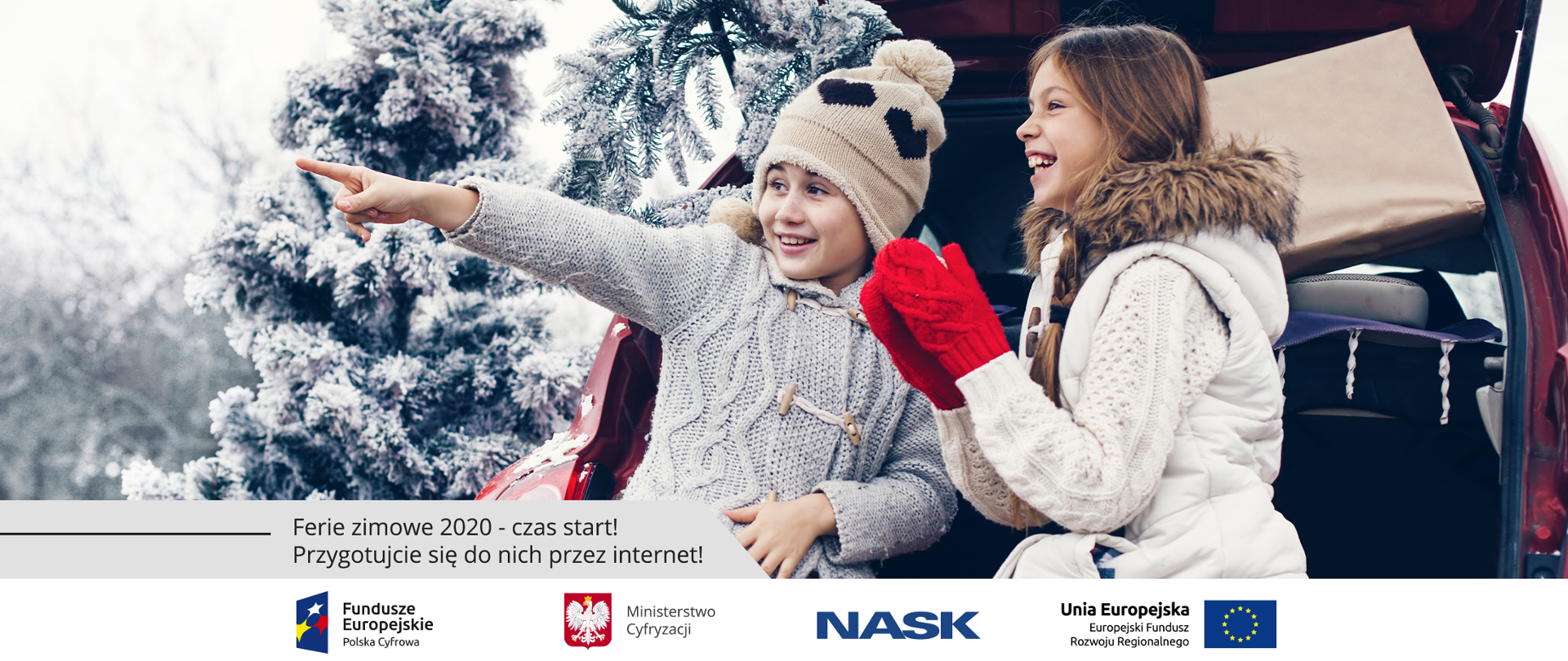 Zimowa aura - samochód stoi obok zaśnieżonych drzew. Dwie dziewczynki siedzą w bagażniku przy otwartej klapie. Obie uśmiechnięte. Jedna w czapce, druga z rękawiczkami. Jedna z nich wskazuje palcem coś w oddali.