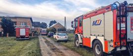 Na zdjęciu samochody strażackie, karetka i samochody cywilne przed posesją, do której do szło do tragedii. W tle zabudowania mieszkalne i gospodarcze.