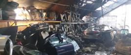 Widać uszkodzone i nadpalone części samochodowe i samochód wewnątrz hali