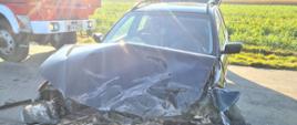 Zdjęcie przedstawia samochód osobowy po wypadku. Auto ma uszkodzony przód i stoi na środku jezdni. 
