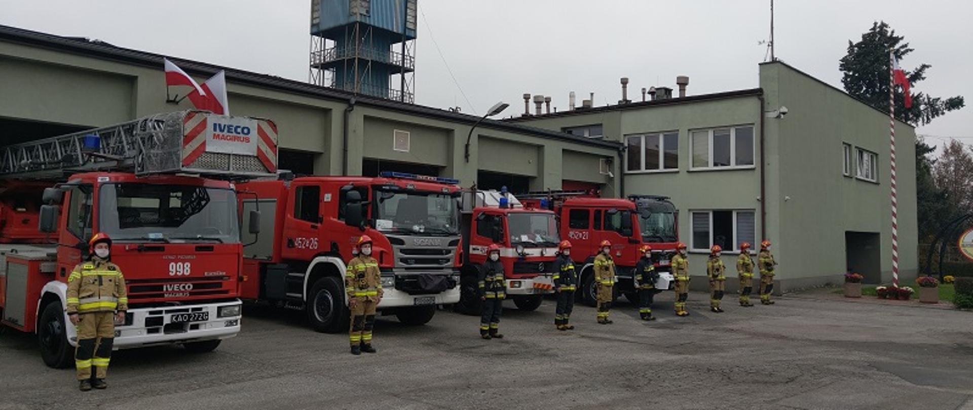 Strażacy w mundurach specjalnych na tle Jednostki Ratowniczo Gaśniczej 