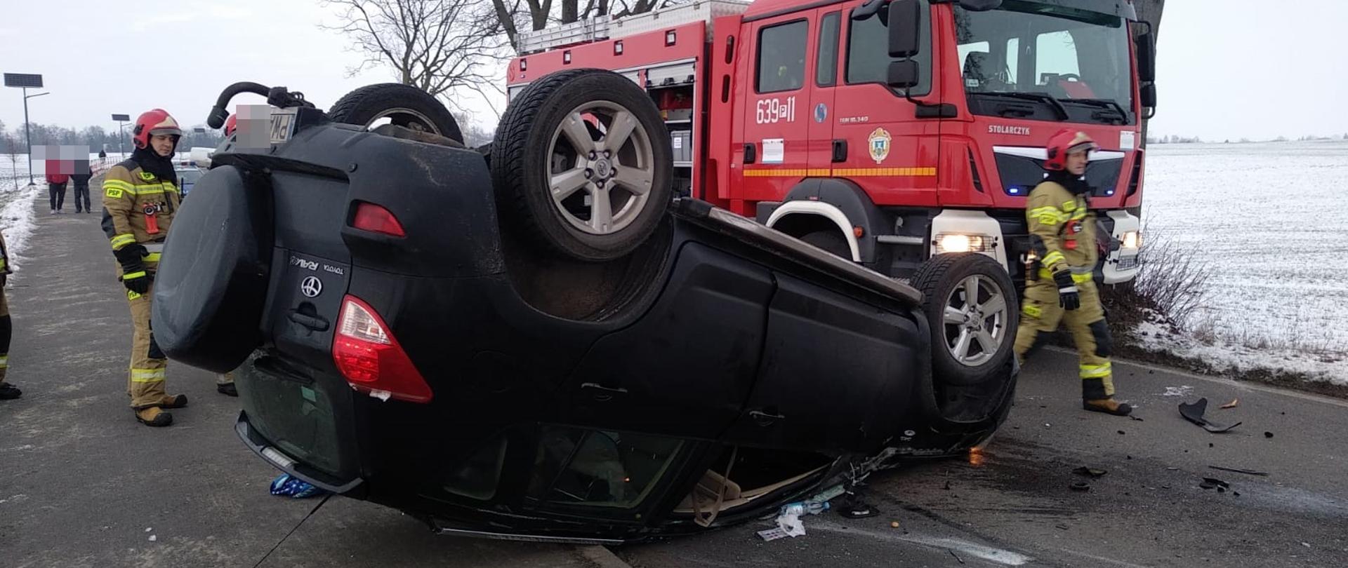 Na zdjęciu widać auto po dachowaniu, strażaków oraz wóz strażacki 