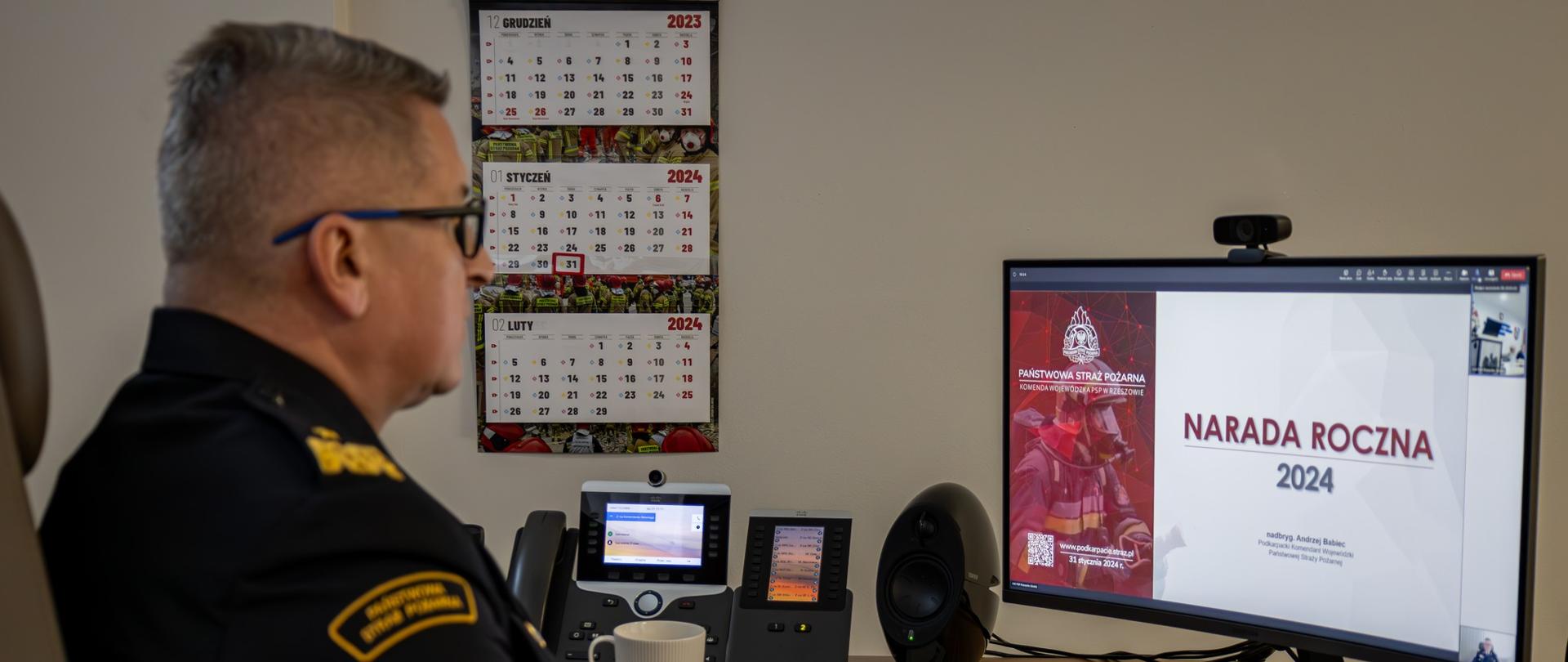 Przy komputerze siedzi nadbrygadier Krzysztof Hejduk, na monitorze widnieje napis narada roczna 2024