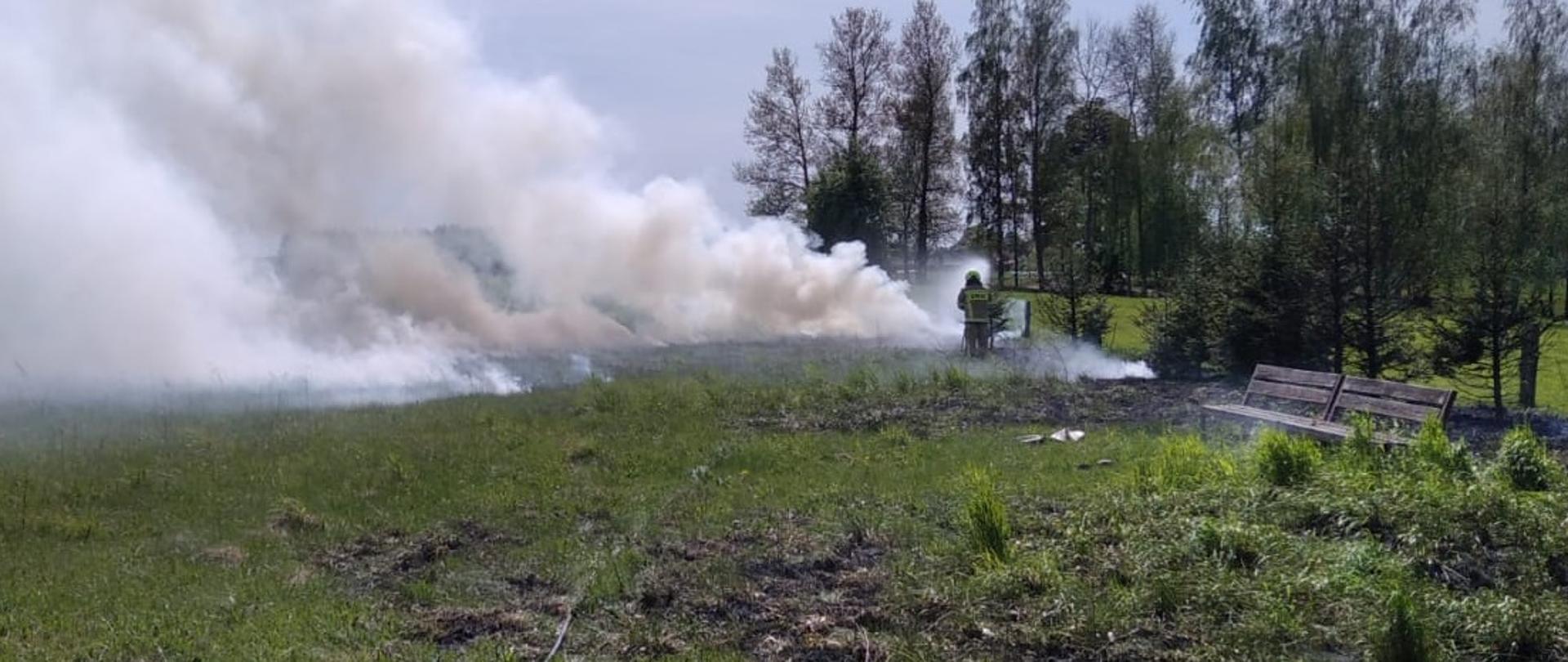 Strażak gasi palącą się trawę na polu. 