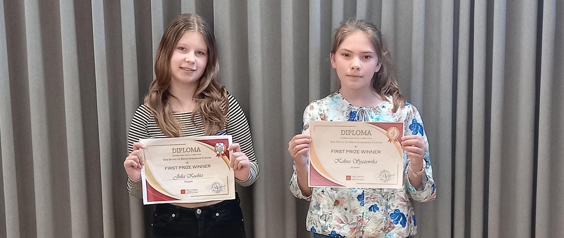 Uczennice ZPSM z dyplomami w ręku na tle szarej kotary