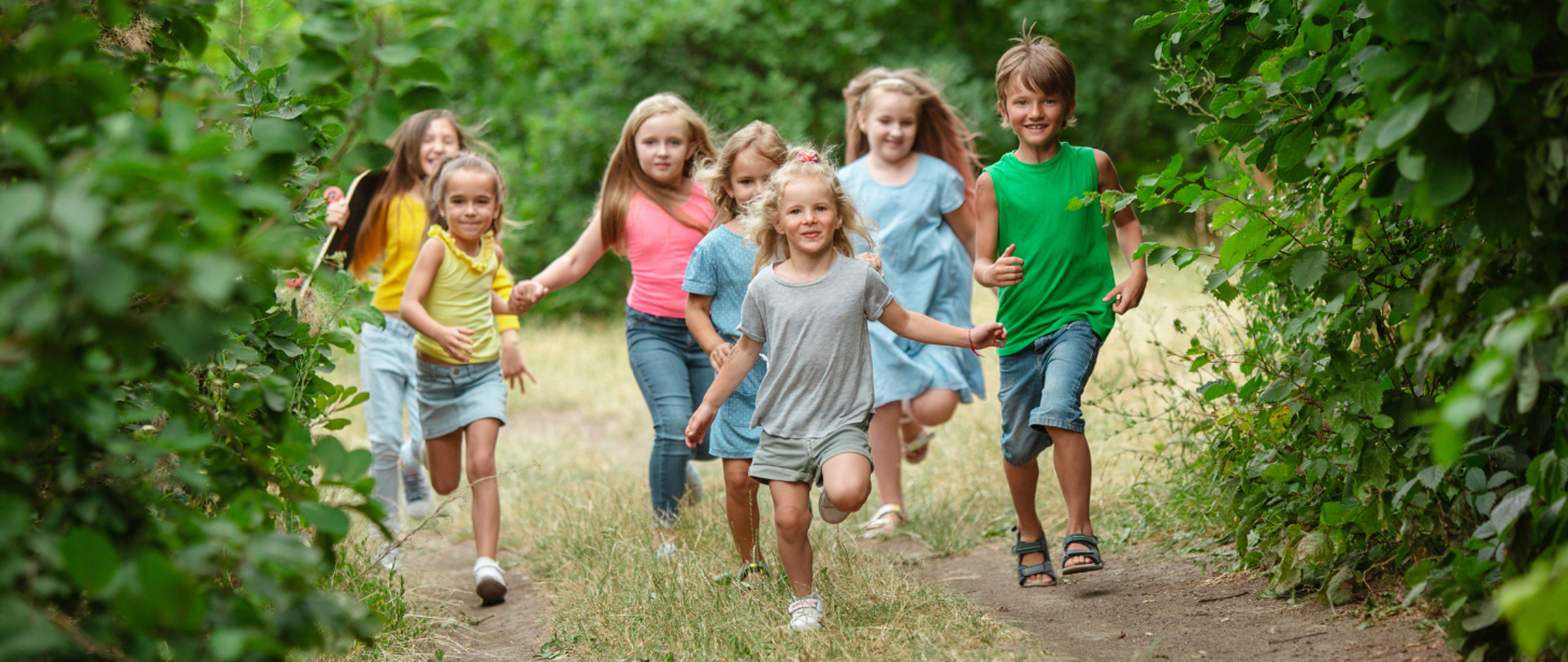 Grupa dzieci biegnie ścieżką wśród drzew i krzewów