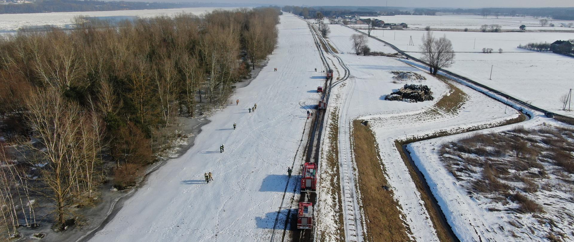 Widok z lotu ptaka. Strażacy oraz pojazdy rozstawione wzdłuż rzeki Wisły