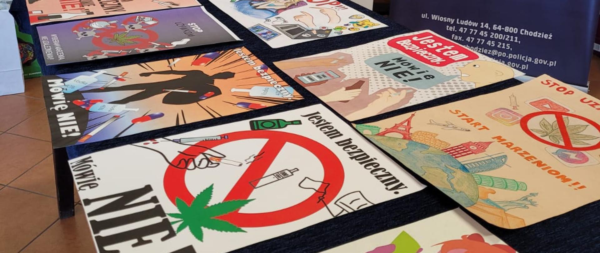 Zdjęcie przedstawia prace laureatów w konkursie "Jestem bezpieczny. MÓWIĘ NIE!" położone na stole.