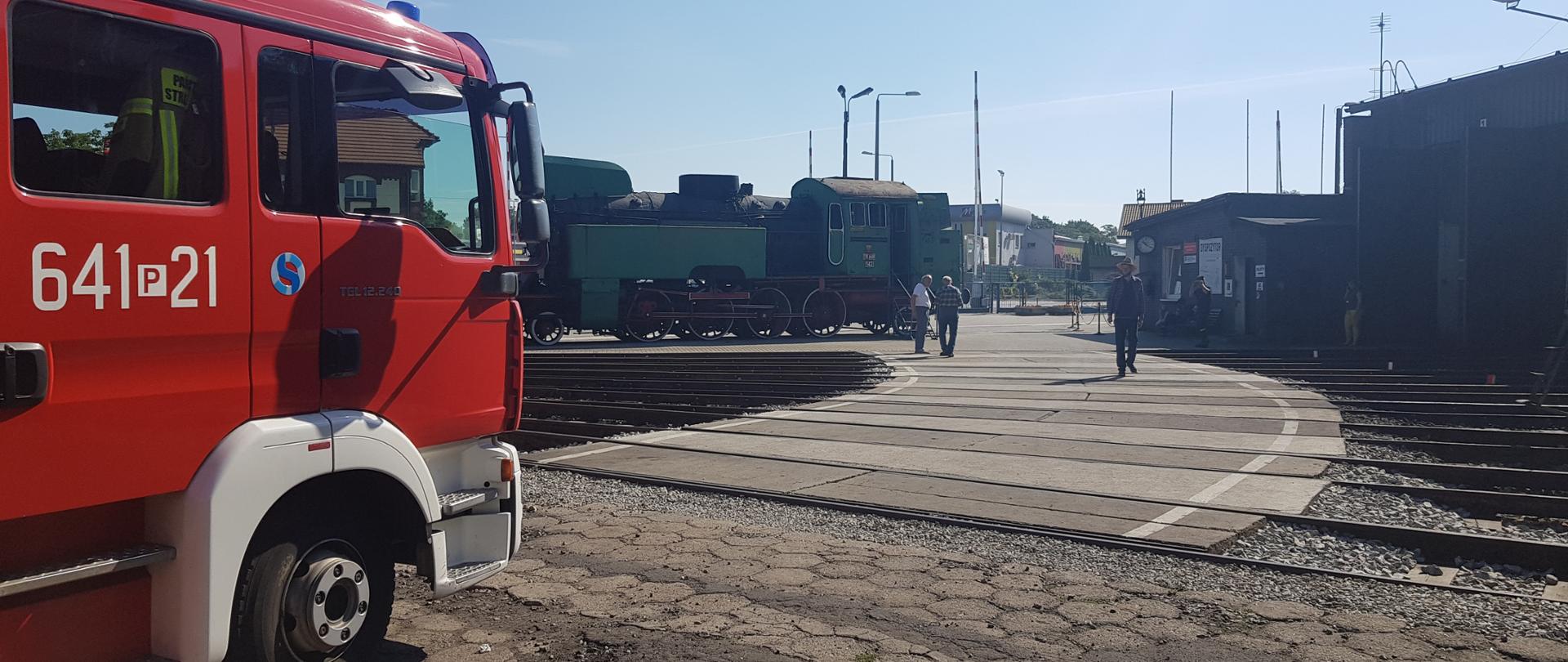 Samochód ratowniczo-gaśniczy wolsztyńskich strażaków pozostawiony w gotowości do wyjazdu podczas przeprowadzanego rozpoznania. W tle, parowozy oraz budynki parowozowni.