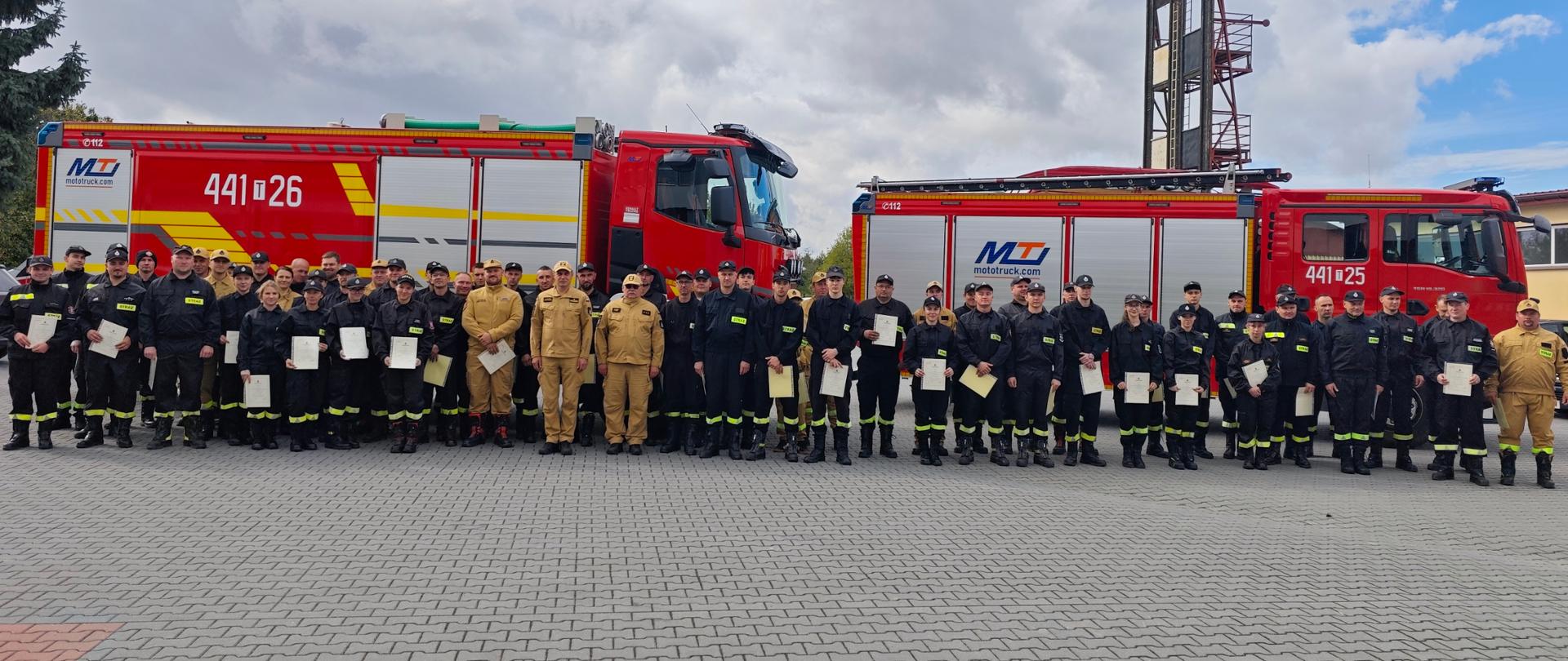 Kierownictwo KP PSP Opatów wraz z uczestnikami kursu OSP na tle samochodów pożarniczych