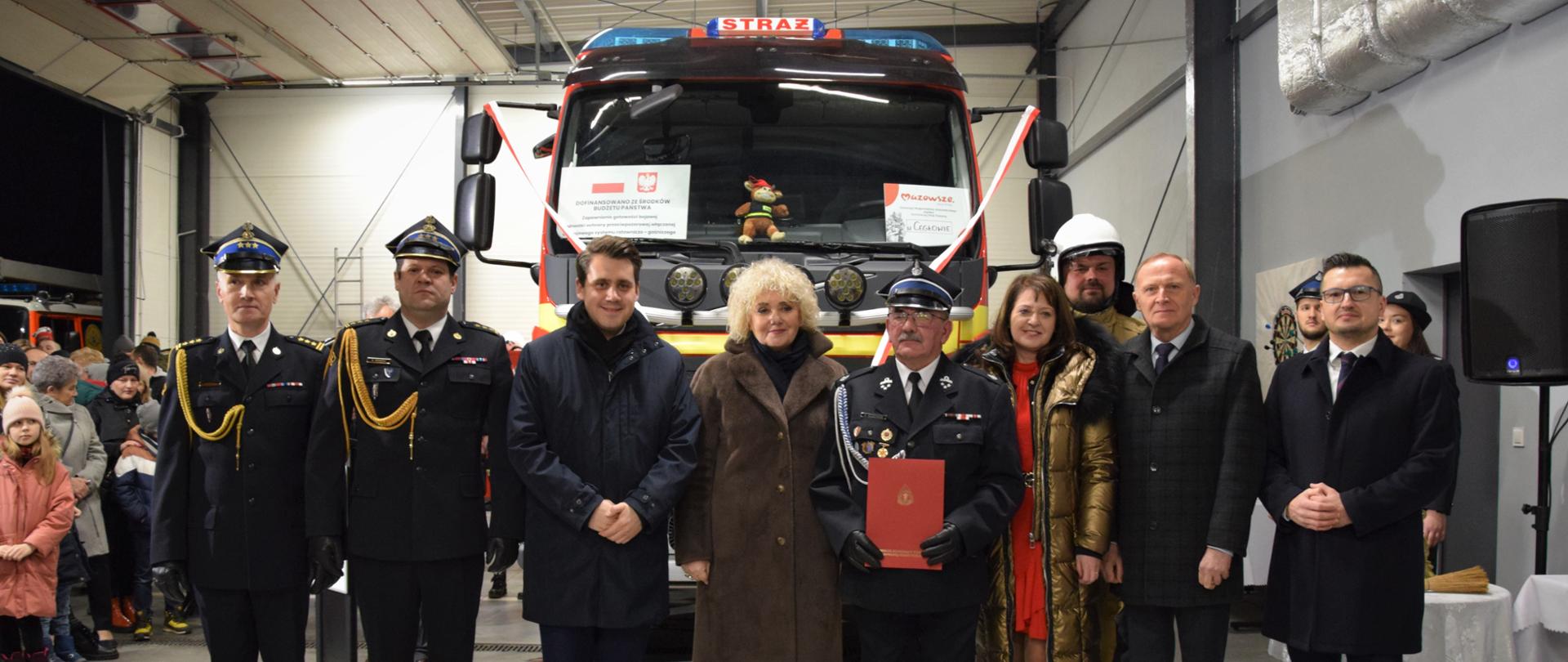 Przedstawiciele PSP oraz parlamentarzyści i Pan Burmistrz stoją wraz z Prezesem i kierowcą OSP Cegłów, za nimi nowy samochód ratowniczo-gaśniczy.