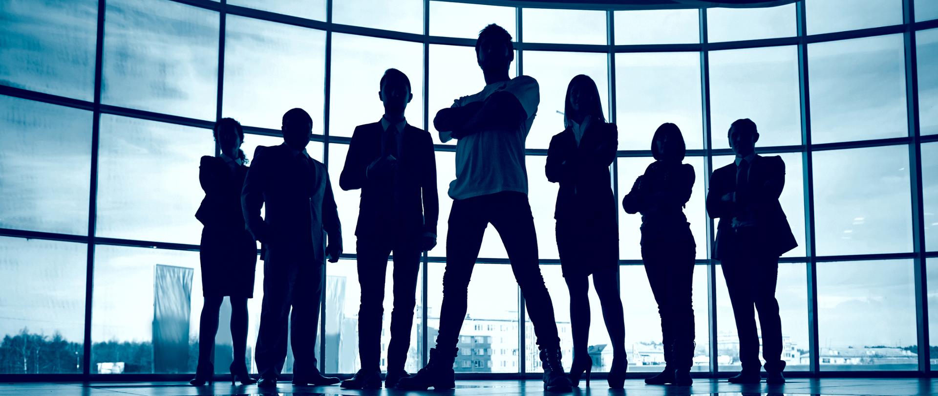 Na zdjęciu jest 7 postaci (kobiety i mężczyźni), w tle przez okna widać budynki i wieżowce.