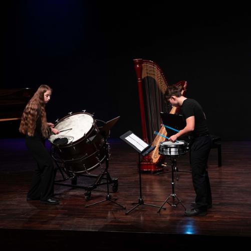 Zdjęcie przedstawia dwoje uczniów wykonujących wspólnie utwór na dwa instrumenty perkusyjne, w tle fortepian i harfa