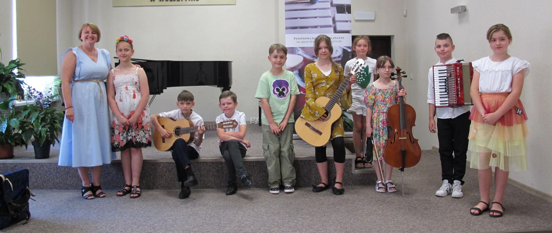 Uczniowie PSM w Wolsztynie, którzy wystąpili na Koncercie Letnim stoją na scenie wraz z panią dyrektor Agnieszką Pilarek-Szumską. Dzieci trzymają instrumenty, na których grały - gitarę, akordeon i wiolonczelę.