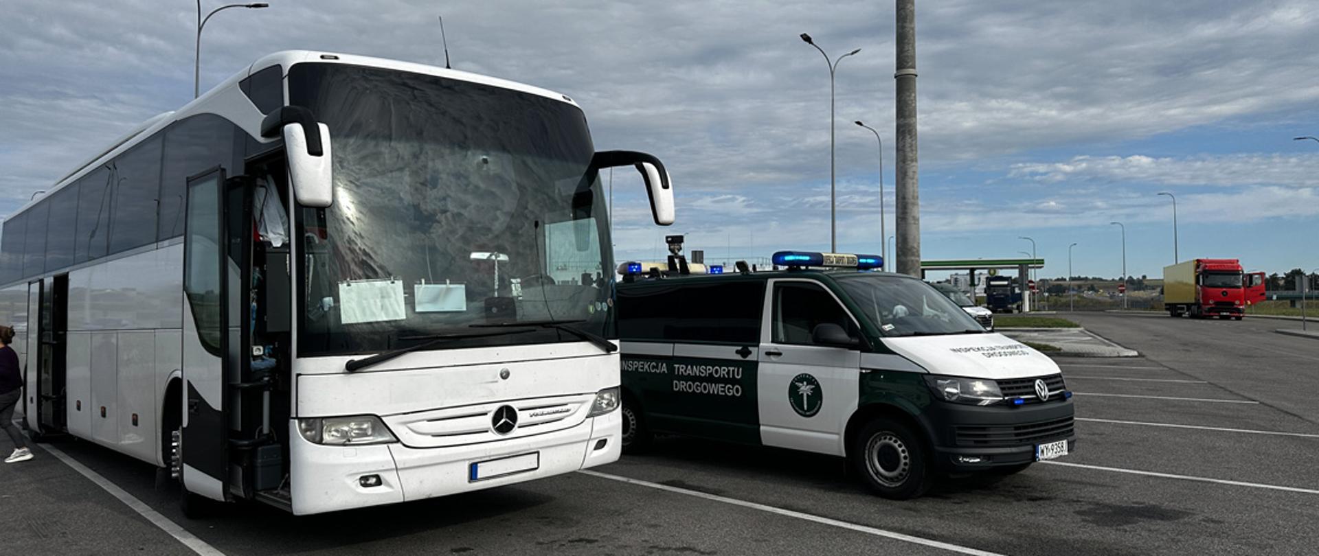 Autobus zatrzymany do kontroli na parkingu, obok którego stoi pojazd służbowy Inspekcji Transportu Drogowego