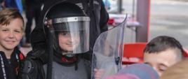 Dziecko na stanowisku edukacyjnym przebrane w strój interwencyjny strażnika więziennego