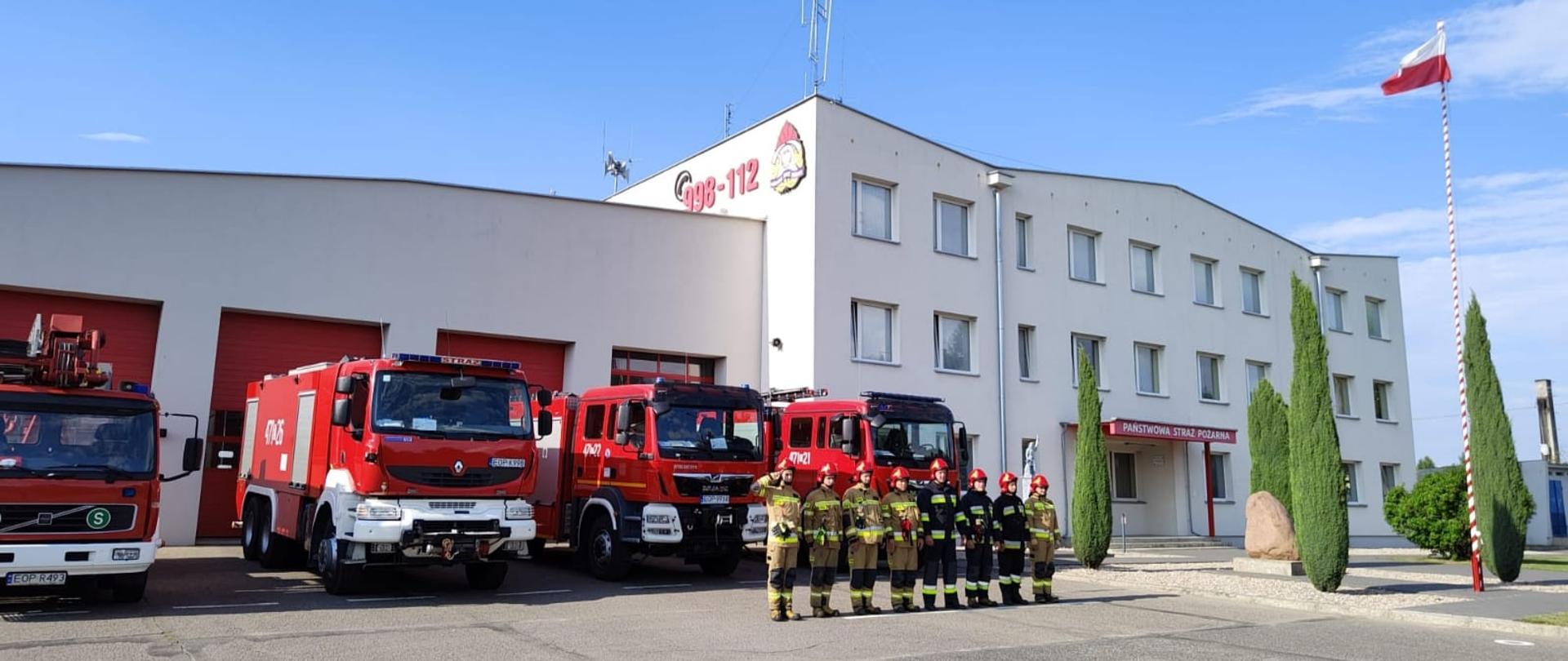Zdjęcie przed Komendą Powiatową PSP w Opocznie przedstawia wystawione wozy bojowe oraz strażaków w umundurowaniu specjalnym oddających honory.