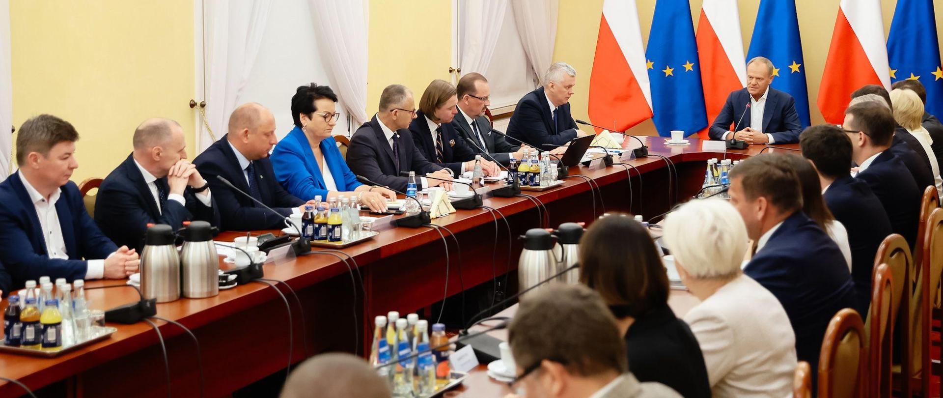 grupa osób siedzi przy okrągłym stole i rozmawia