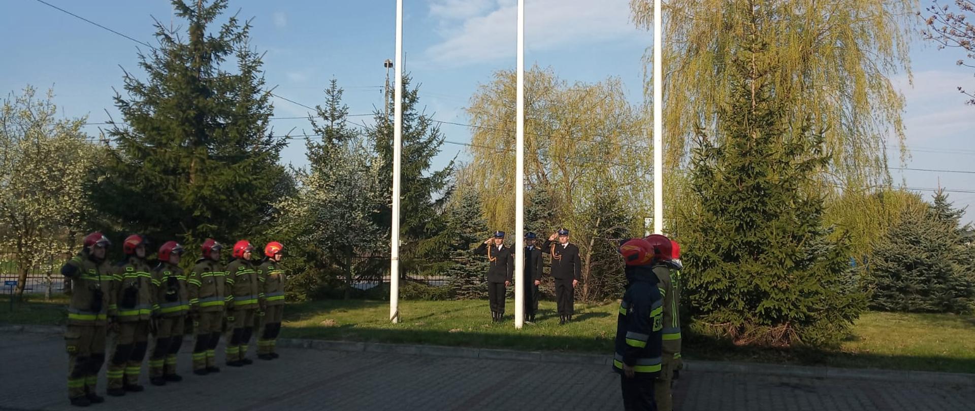Strażacy stający przed budynkiem podczas wciągania flagi