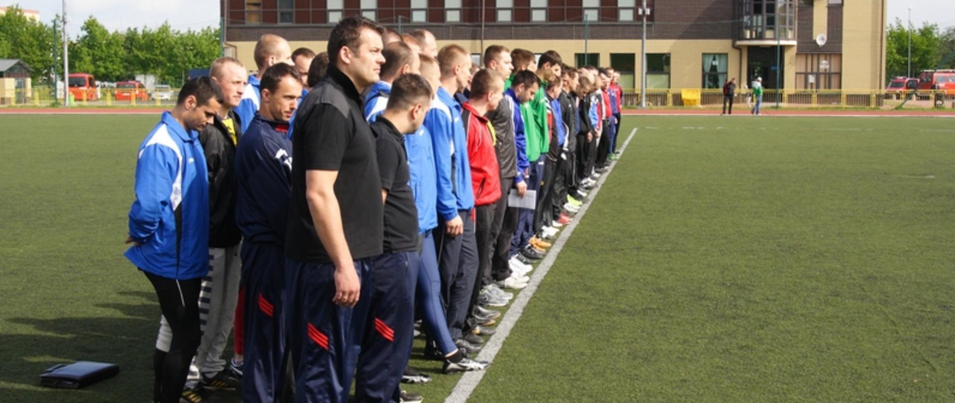 Zdjęcie przedstawia drużyny w szeregu na boisku