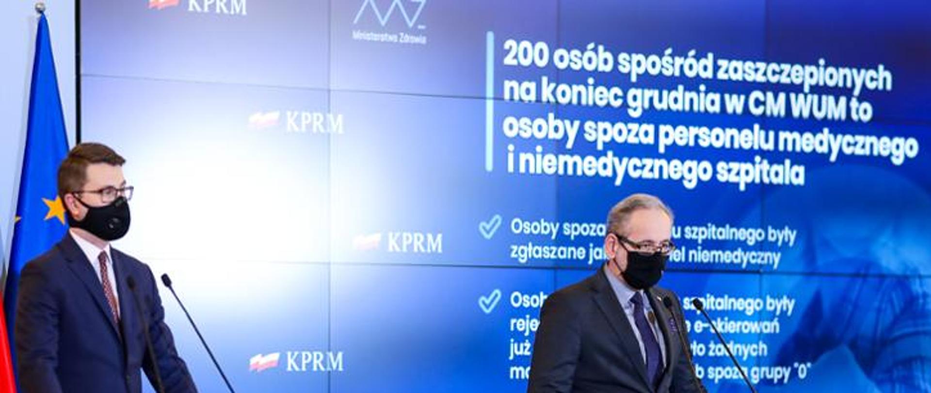 Rzecznik Rządu i Minister Zdrowia podczas konferencji. Stoją przy mikrofonach. W tle ścianka, na której wyświetlane są informacje dotyczące tematu konferencji.
