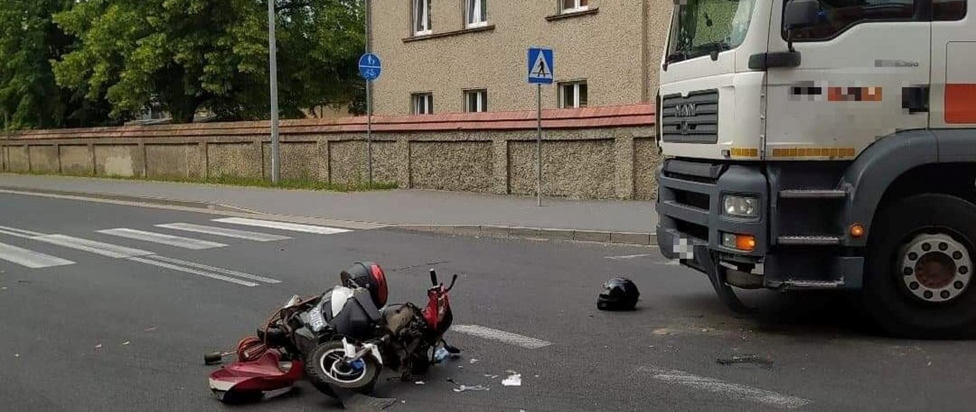 Widać skuter leżący na drodze, po prawej samochód ciężarowy