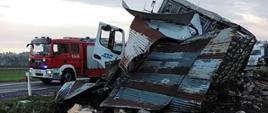 Rozwalona naczepa, w tle samochód strażacki stojący na jezdni