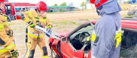 Zdjęcie przedstawia ćwiczenia straży pożarnej na punkcie kasacji pojazdów, strażacy ubrani w ubrania specjalne oraz hełm, używają narzędzi hydraulicznych do cięcia pojazdów